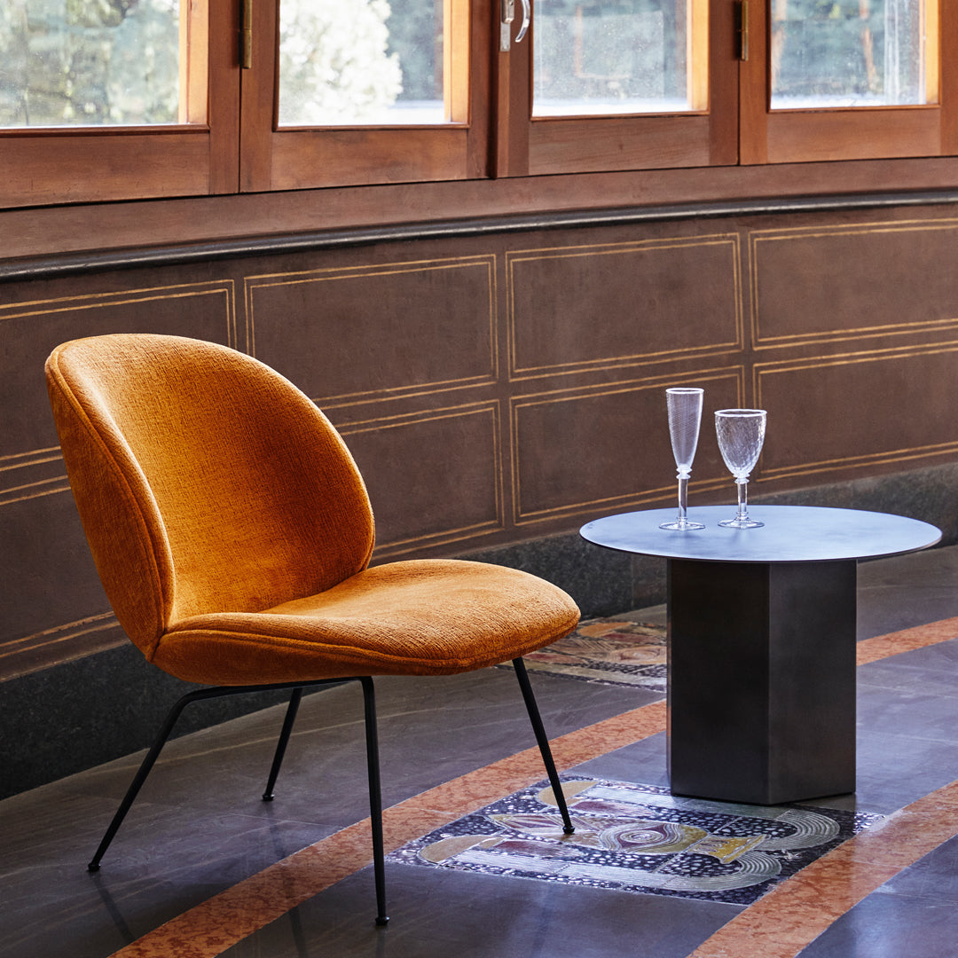Velvet orange chair with sleek black legs, paired with a round gray table on a patterned floor.