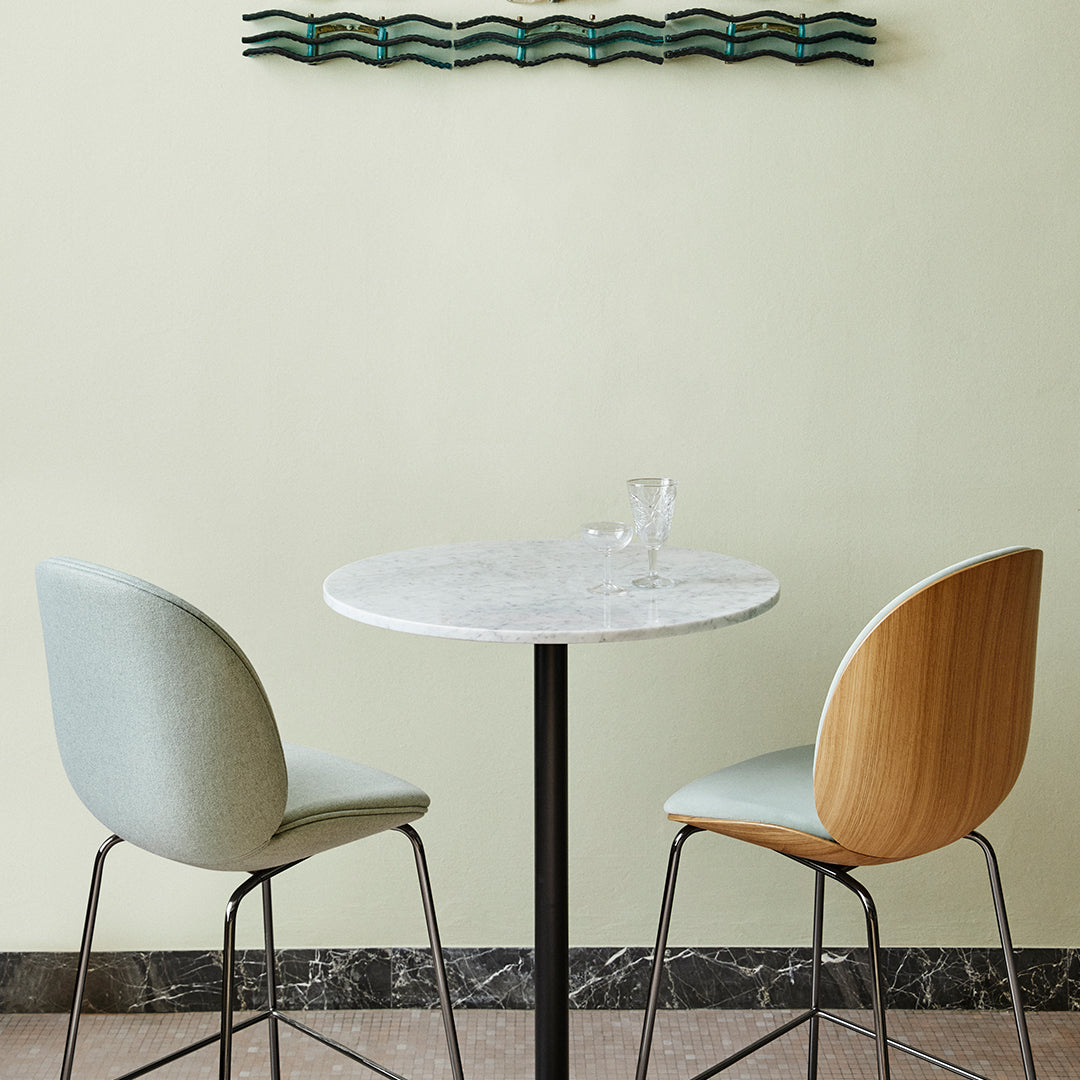 "Soft pastel blue and natural wood dining chairs around a white marble table, set against a muted green wall."