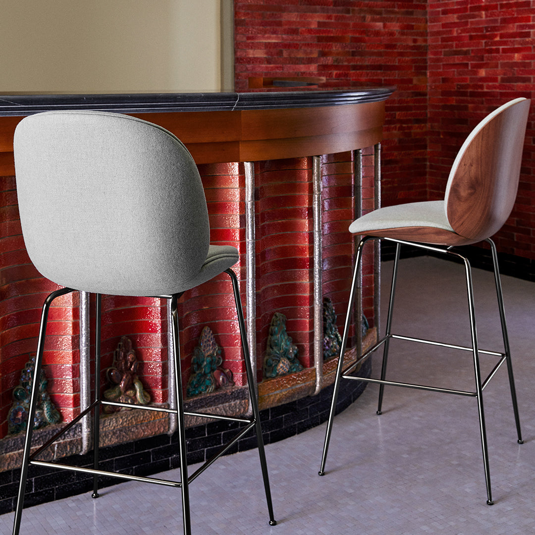 "Gray upholstered bar stool with a sleek wood back and black metal legs, paired with a walnut-finished stool."