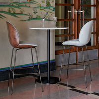 Modern bar table with a round white top; stylish chairs in light grey and warm brown leather tones, set against a colorful patterned backdrop.