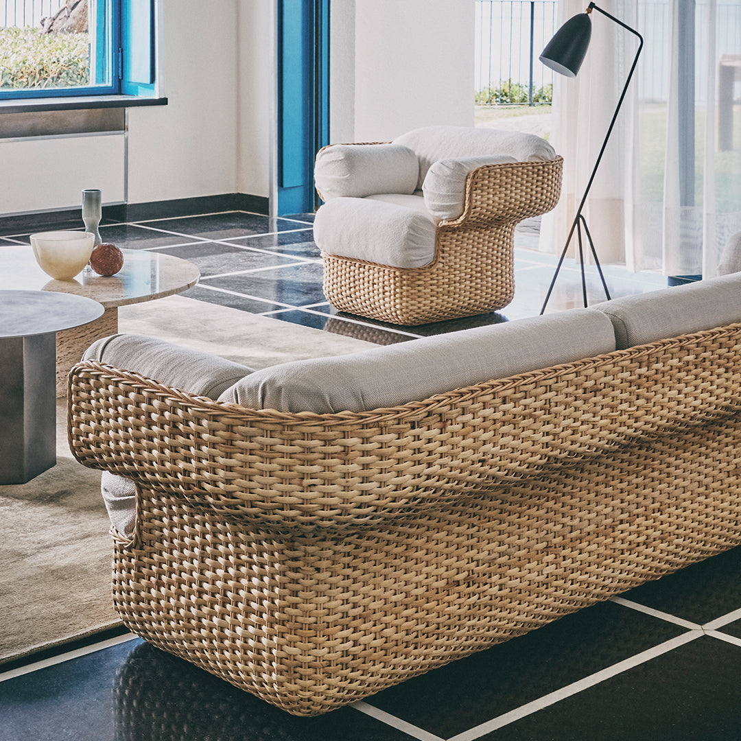 Woven rattan sofa with light gray cushions, accented by a sleek black and white patterned floor.