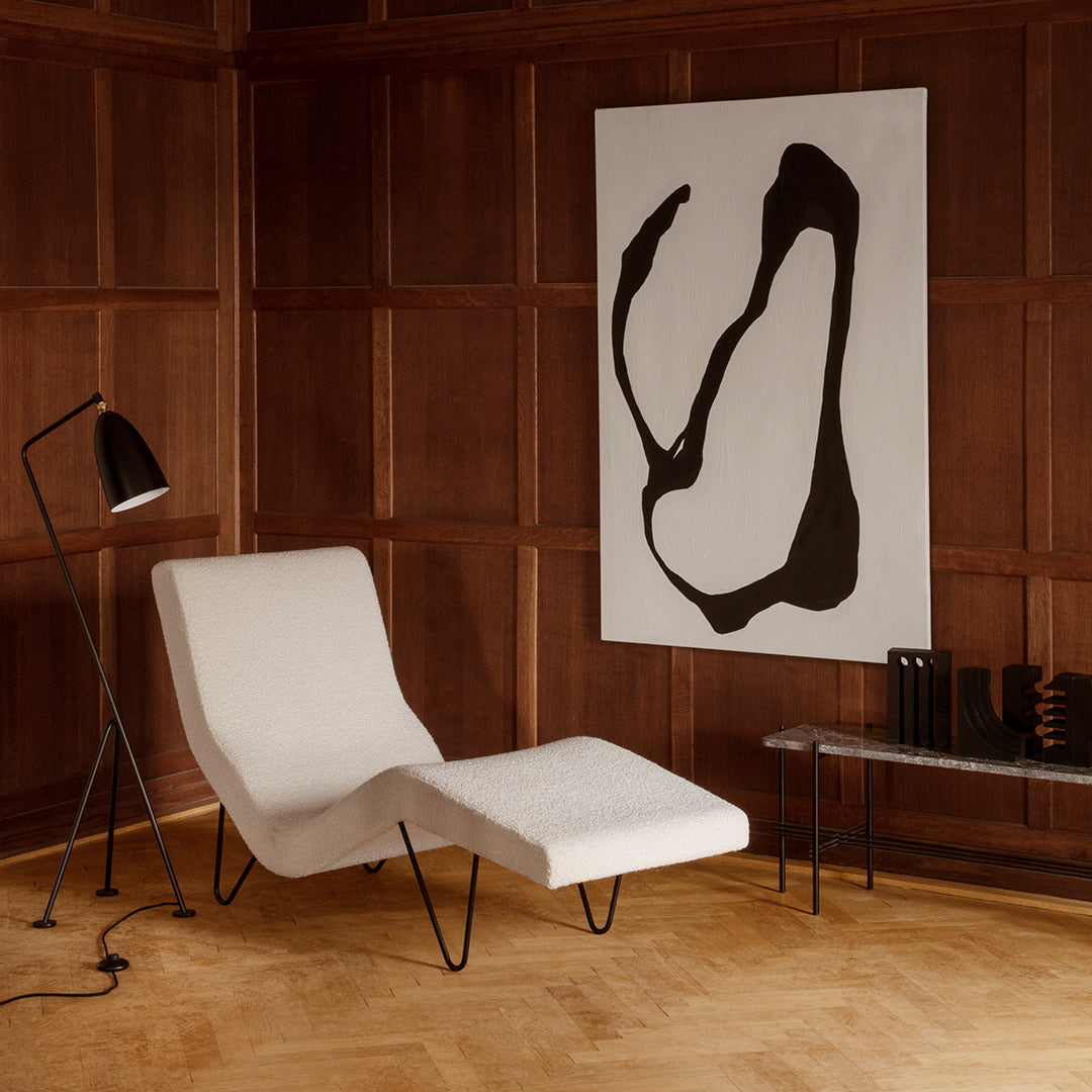 Modern white lounge chair with black accents, set against warm wood paneling and abstract black and white wall art.
