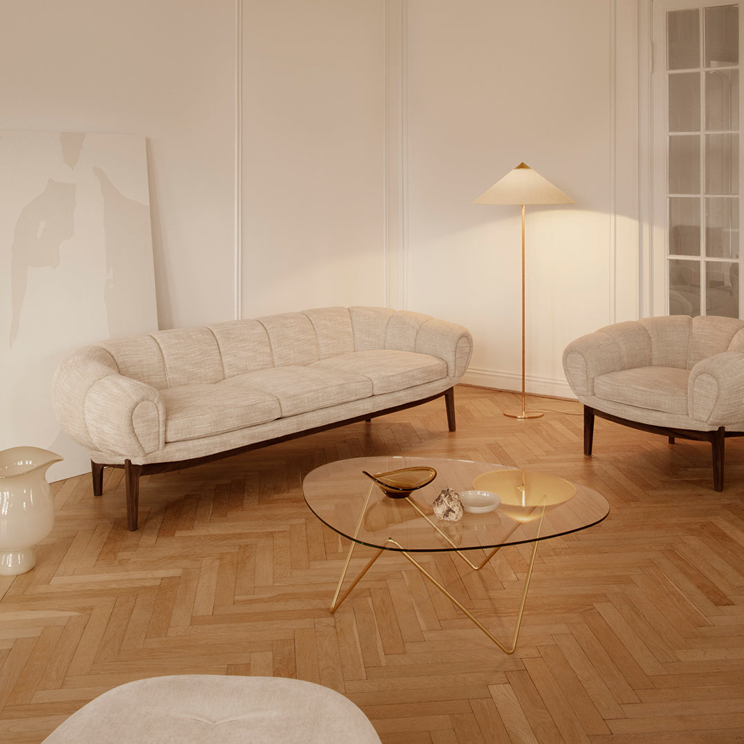 Beige upholstered sofa and armchairs with a light wood floor and clear glass coffee table, creating a warm, inviting space.
