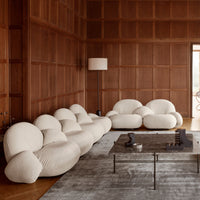 Cozy cream-colored sofa with soft, rounded shapes, complemented by a gray rug and warm wood paneling in an elegant interior.
