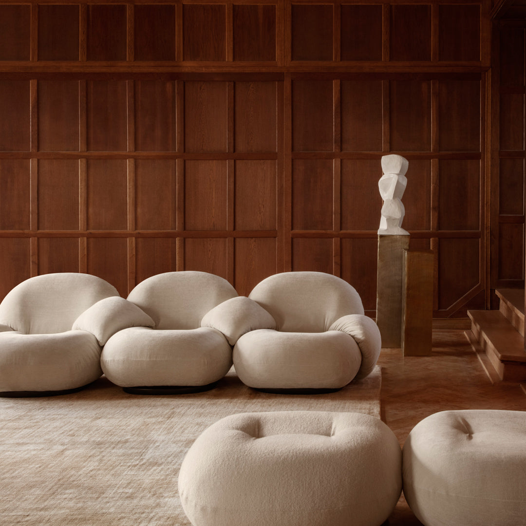 Beige plush sofa set with rounded shapes, complemented by a light beige area rug and rich wooden paneling backdrop.