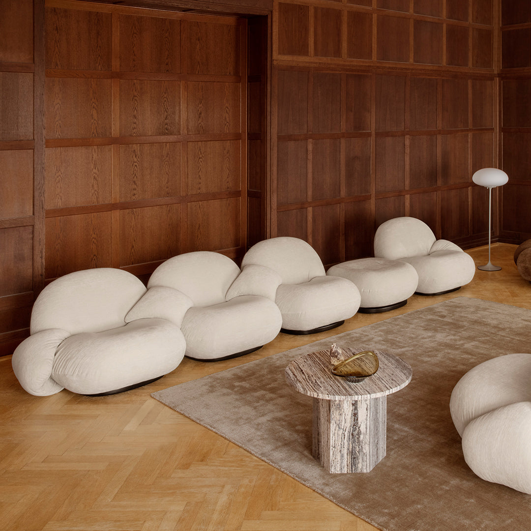 Soft beige organic shapes sofa against a warm wood-paneled wall, complemented by a neutral rug and silver table.