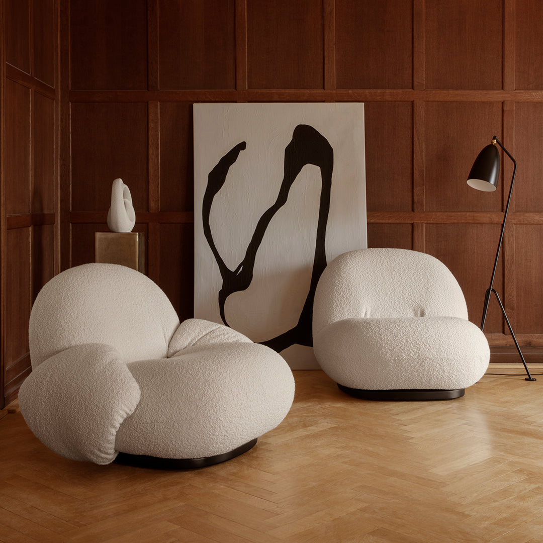 White textured chairs with organic shapes, set against a dark wood backdrop and abstract black-and-white artwork.