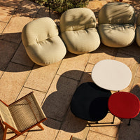 Set of cozy, curved chairs in soft green and cream, paired with modern tables in white, black, and red on a sunny patio.