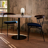 Modern round table with a white marble top, paired with black and blue patterned chairs. Earthy wall backdrop.
