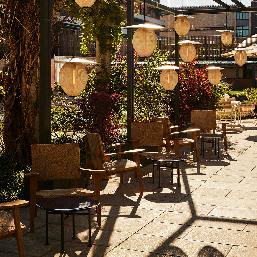 "Stylish wooden chairs in a sunny outdoor setting, surrounded by green plants and warm hanging lanterns."