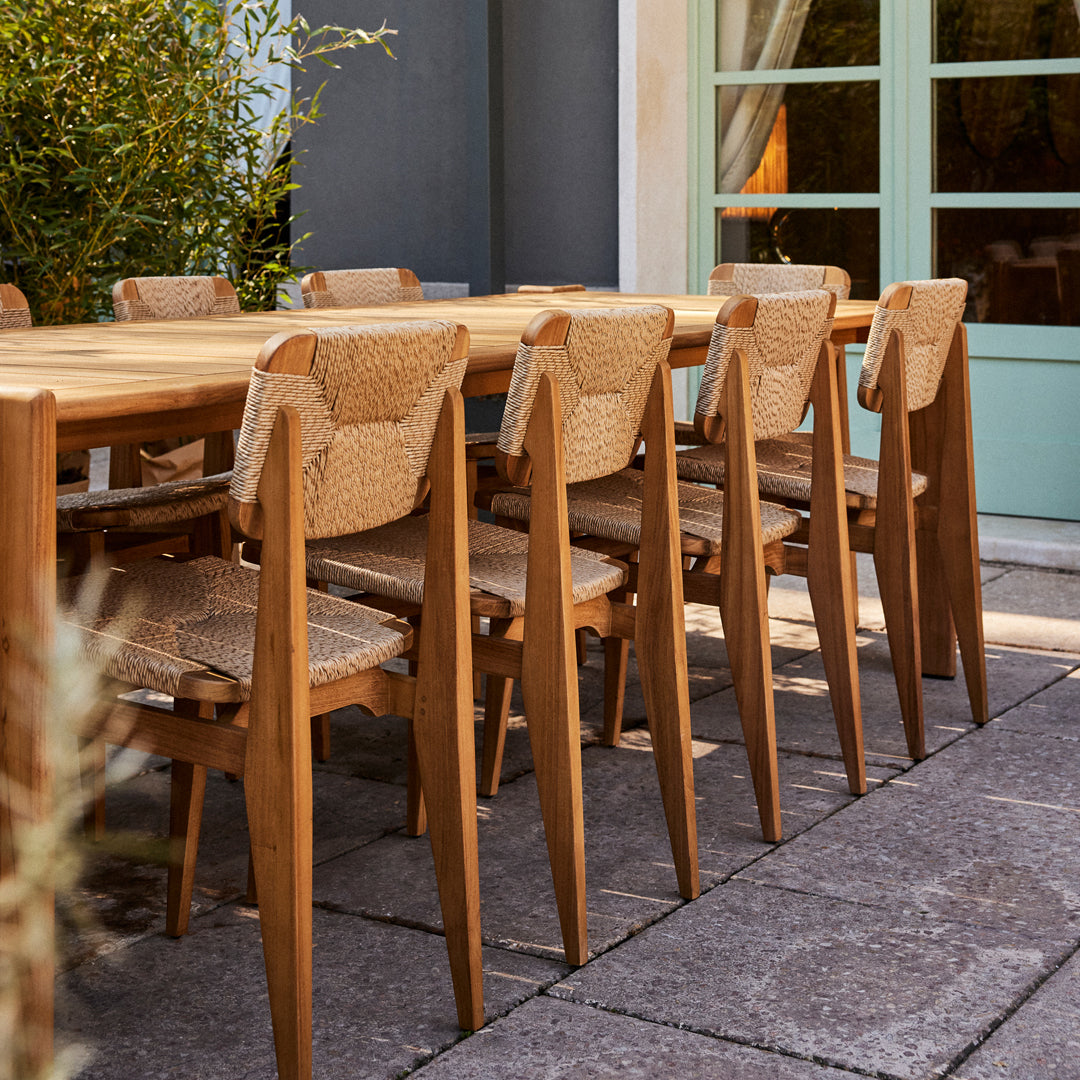"Natural wooden dining chairs with woven seats, set against a light blue door and paved patio."
