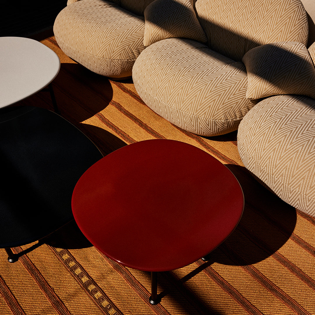 Red, black, and white round coffee tables on a warm striped rug with beige textured cushions in a modern living space.