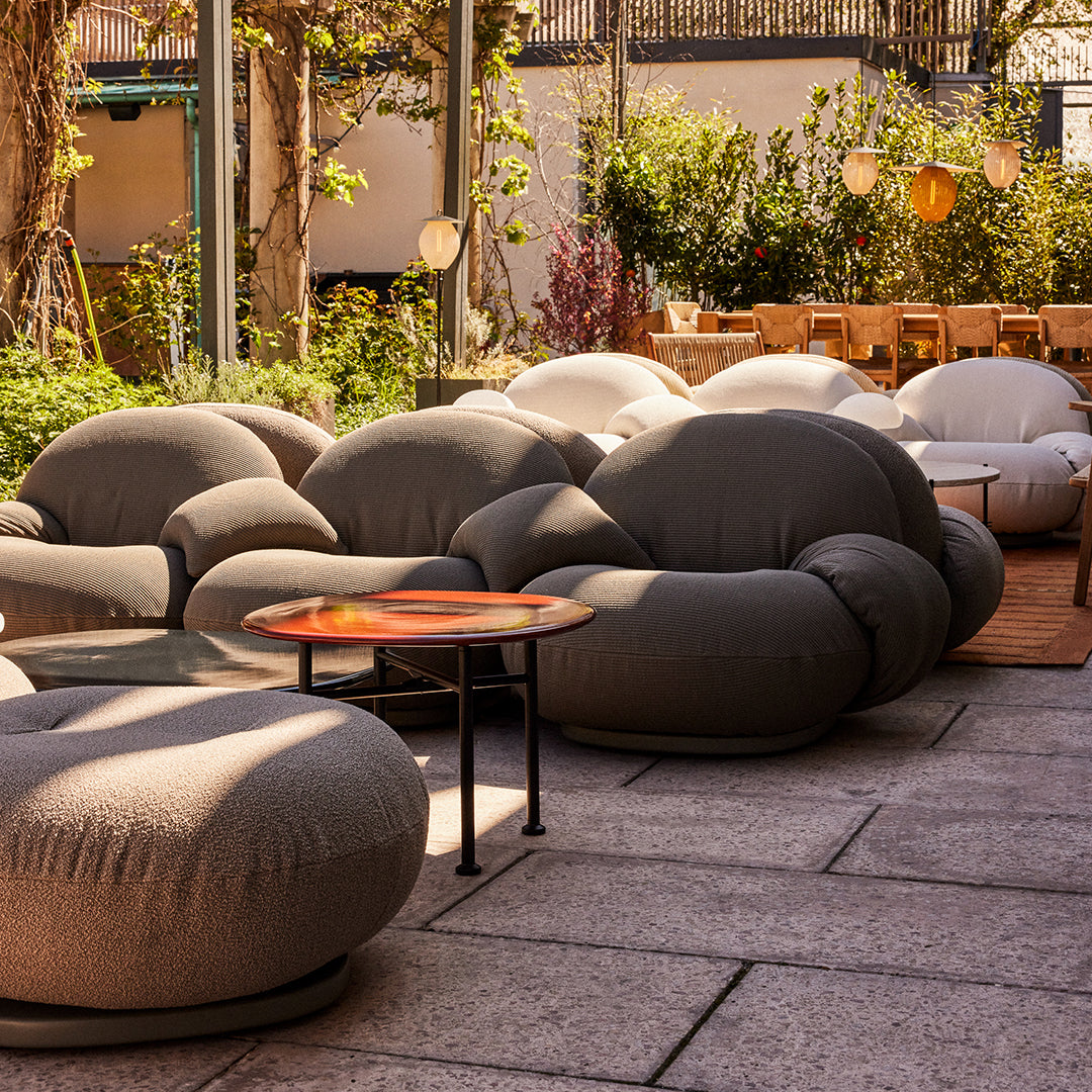 Cozy, rounded outdoor seating in warm gray tones with soft textures, complemented by a stylish wooden table on a patio.