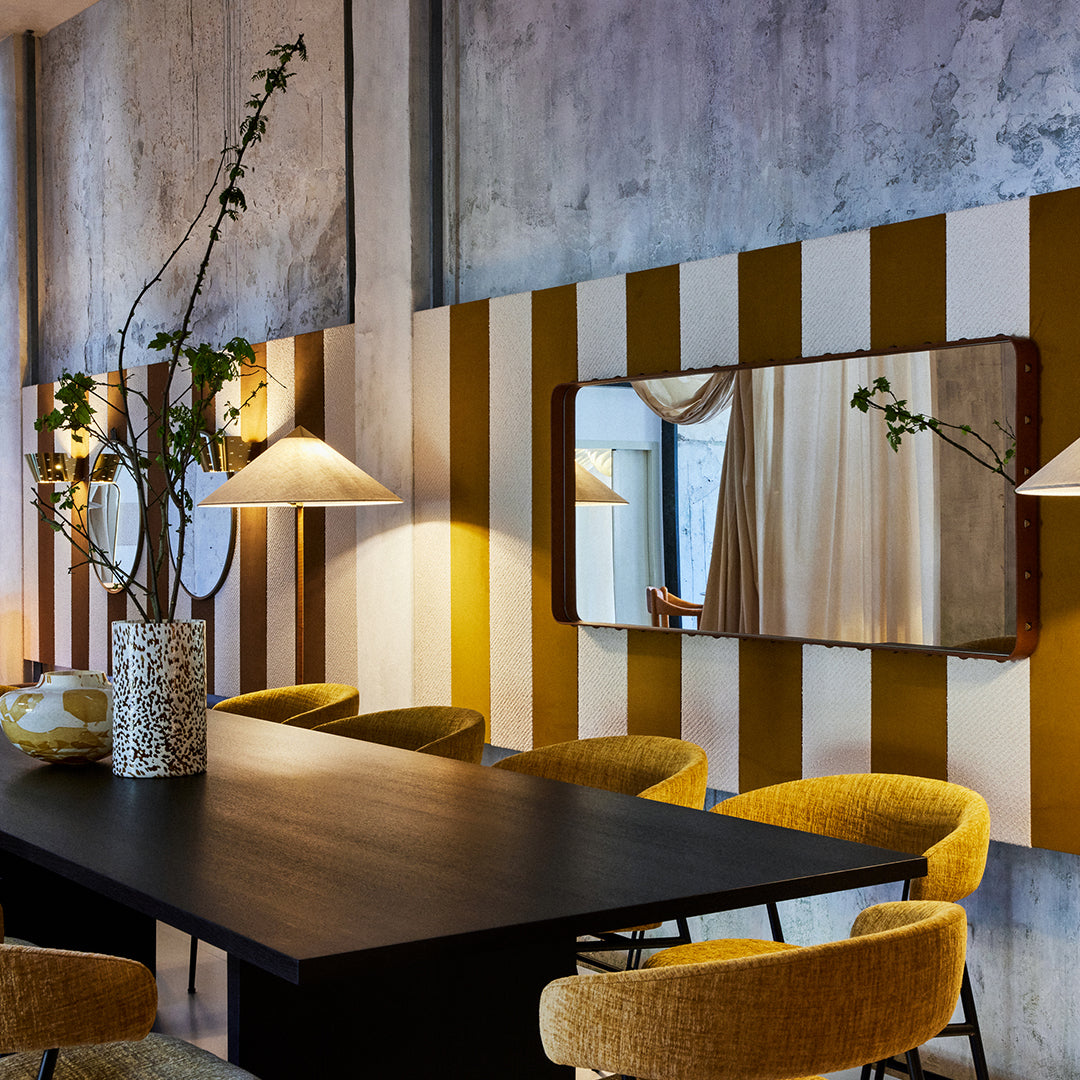 "Modern dining space featuring mustard yellow and cream striped walls, dark table, and soft yellow chairs."