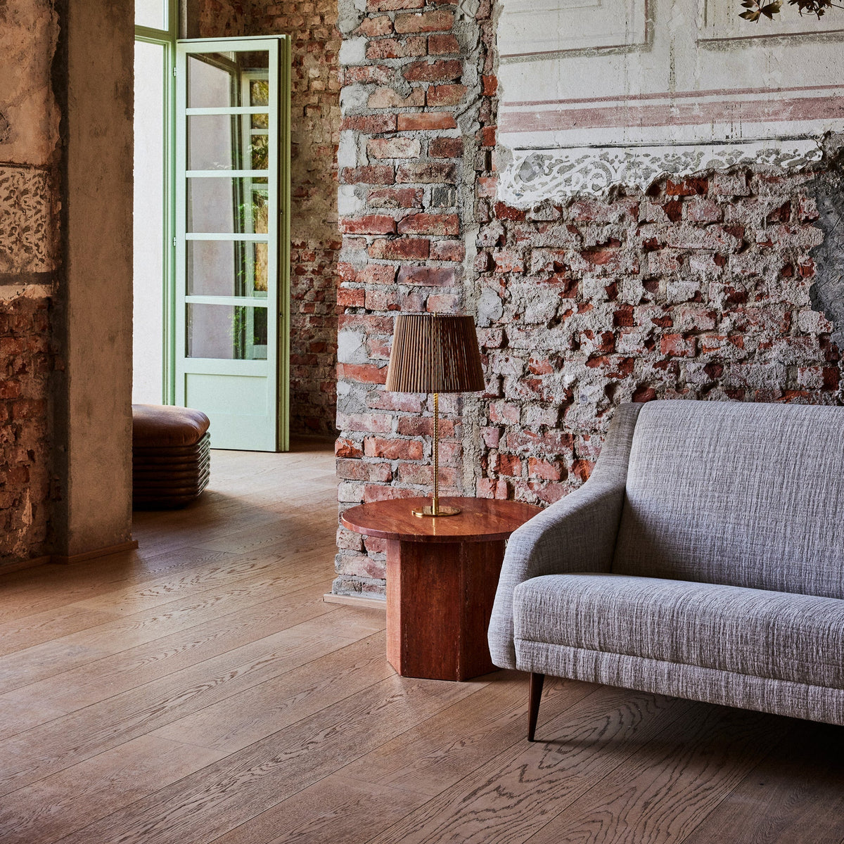 Gray sofa with subtle texture, warm wooden table, and rustic brick wall in a cozy interior setting.