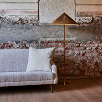 Stylish beige sofa with a textured pattern, paired with a gold lamp featuring a triangular shade against a rustic brick wall.