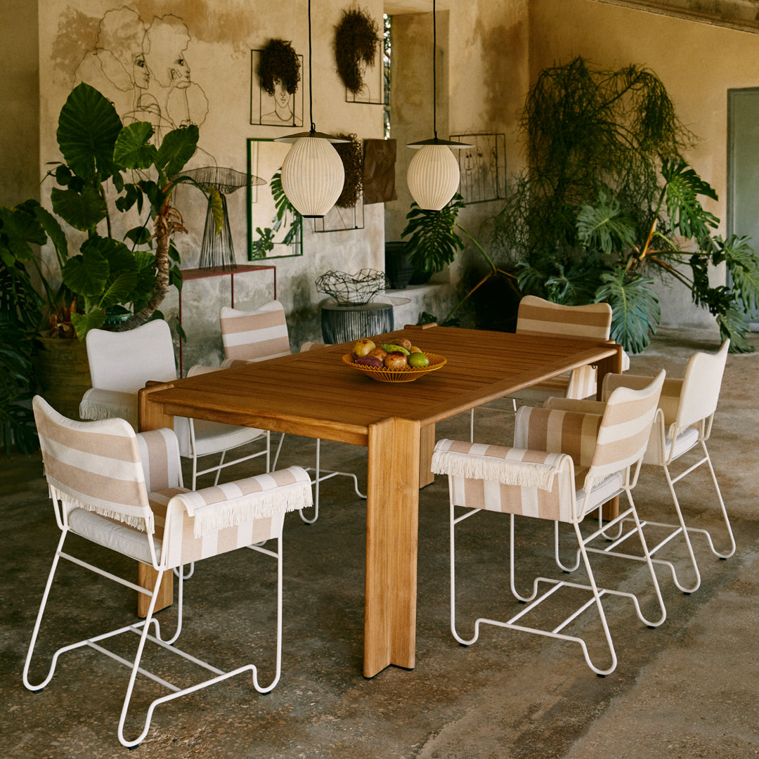 Wooden dining table with striped beige and white chairs, complemented by lush greenery in a modern outdoor setting.