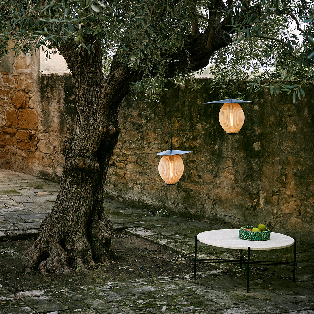"Warm amber pendant lights under an olive tree, contrasting with rustic stone wall and green table centerpiece."