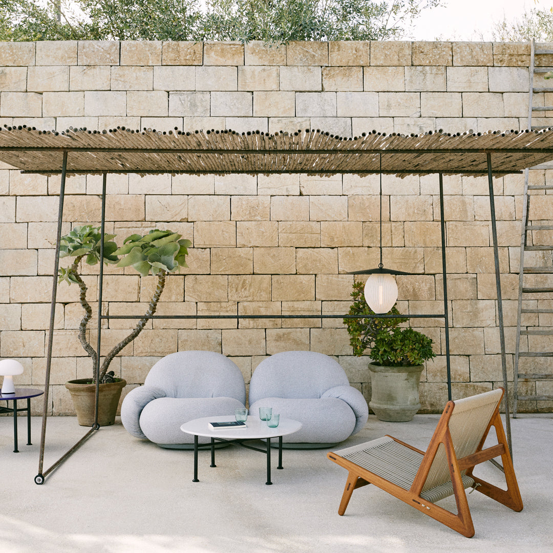Light blue seating with organic shapes, brown wooden accents, and a textured overhead cover against a stone backdrop.