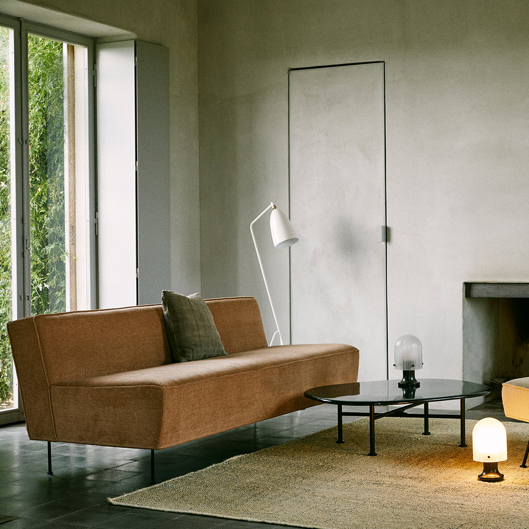 Sofa in warm brown fabric with a minimalist design, complemented by a neutral-toned rug and modern lighting.