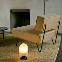 Beige upholstered chair with minimalist black metal frame, set on a textured beige rug against a neutral backdrop.