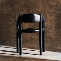 Black wooden chair with a minimalist design, smooth surface and elegant curves against a textured backdrop.
