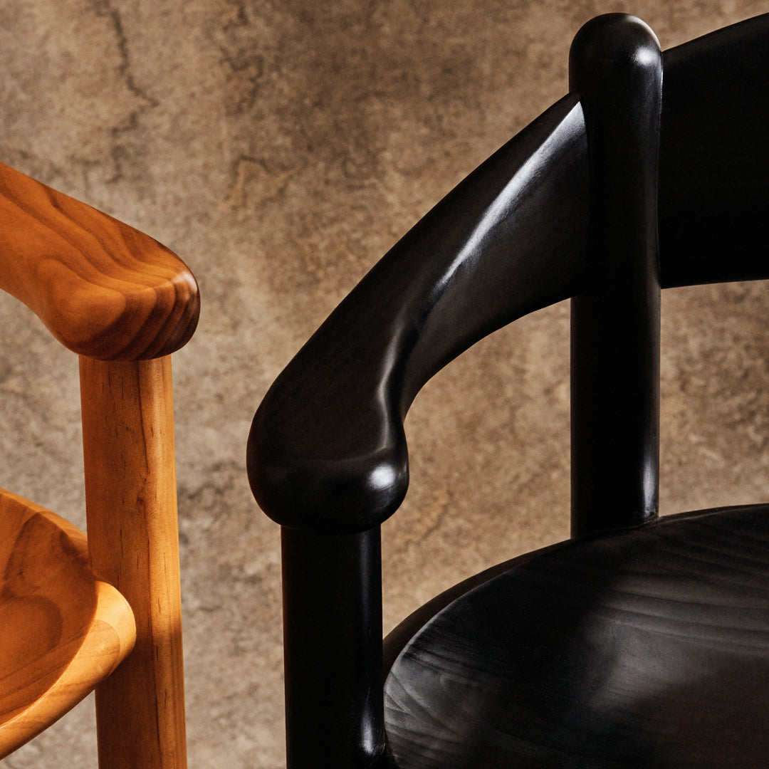 Black and natural wood chair arms with smooth curves against a textured gray background.
