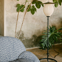 Blue and white chevron patterned sofa beside a sleek black lamp and lush green plant against a textured wall.