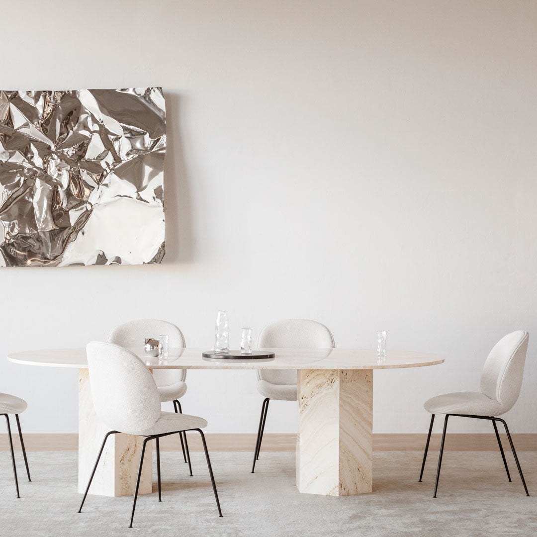 Round dining table with a polished marble base and white chairs, set against a minimalist, textured silver wall art.