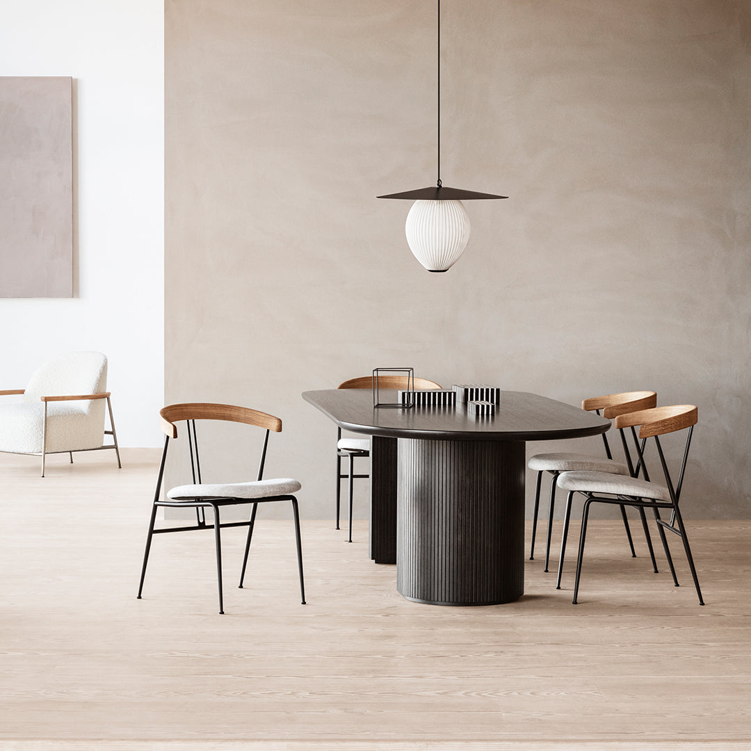 Modern dining table with a sleek black finish, surrounded by light wood and white upholstered chairs against a soft beige backdrop.