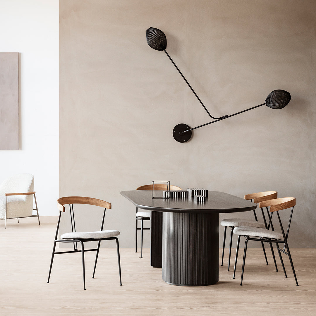 Modern dining room featuring a sleek black table, light wooden chairs, and minimalist decor against soft beige walls.