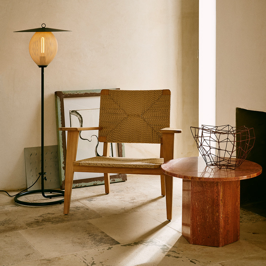 Wooden chair with a woven tan seat, round marble table with warm brown tones, and soft beige backdrop. Elegant geometric patterns.