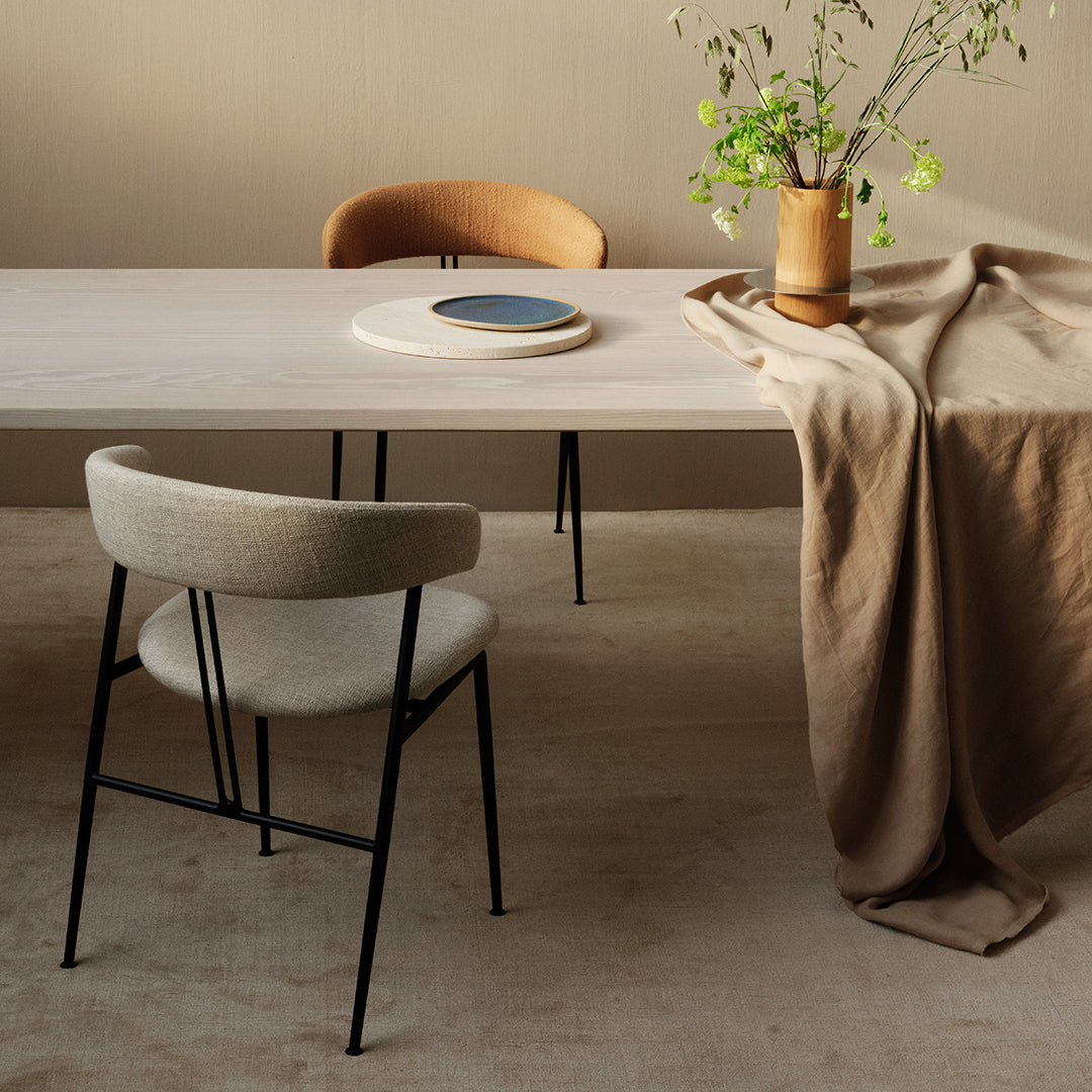 Minimalist dining setup featuring beige table, brown chairs, and a soft brown table runner with a blue accent plate.