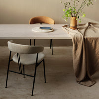 Minimalist dining setup featuring beige table, brown chairs, and a soft brown table runner with a blue accent plate.