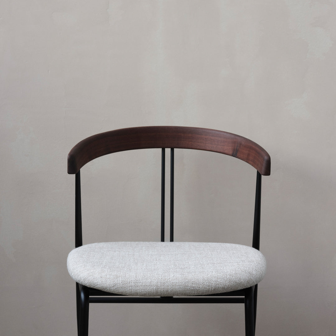 Minimalist chair with a dark wood curved backrest and light gray fabric seat against a neutral background.