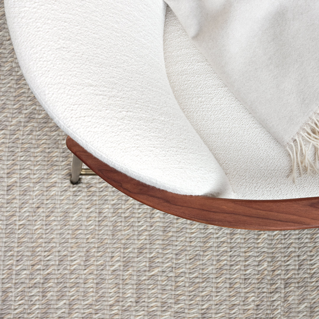 White textured chair on a neutral woven rug, featuring soft patterns and warm wood accents.