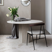 Elegant round marble table with soft gray drapery and a minimalist black metal chair. Neutral color palette with green accents.