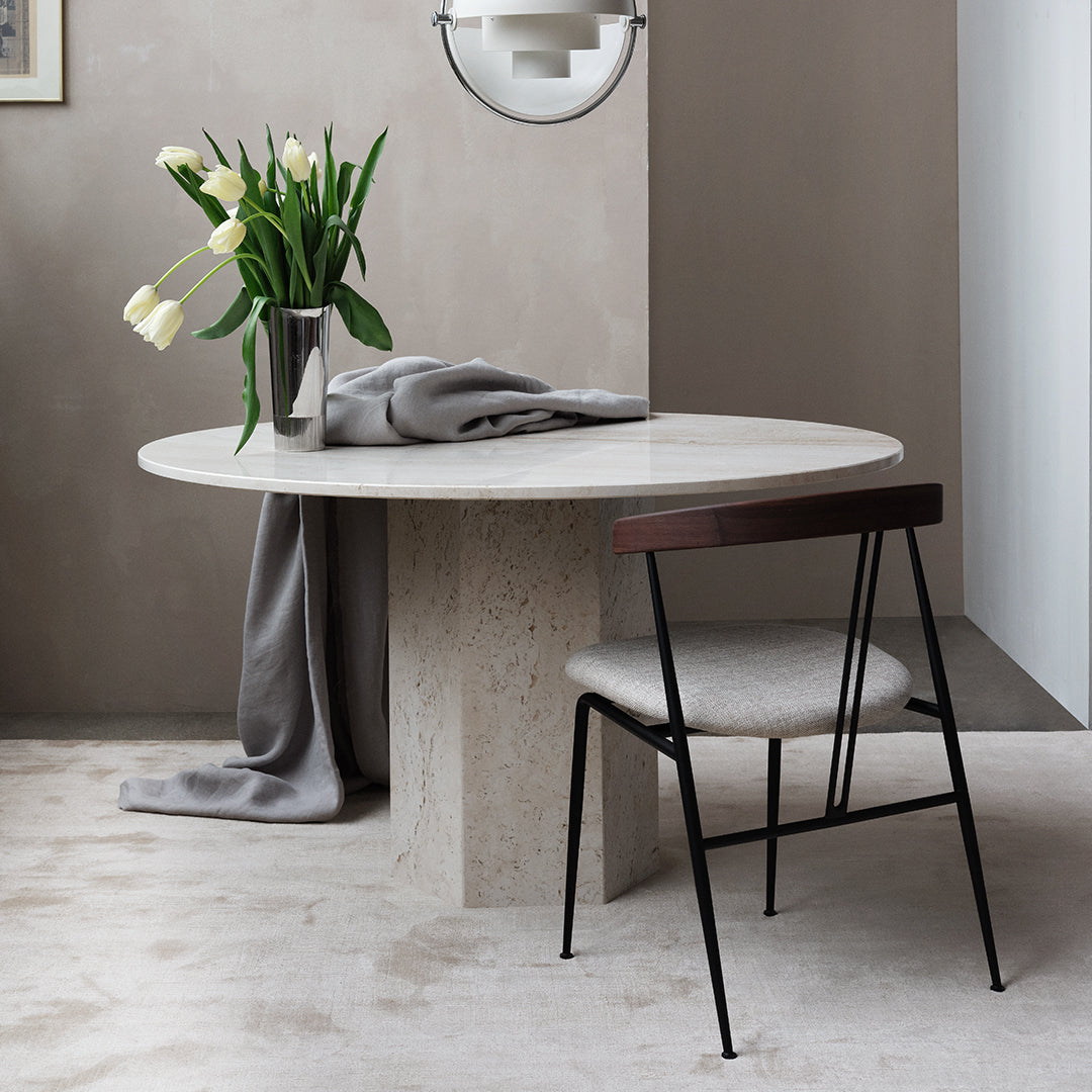 Elegant round marble dining table with a neutral gray tablecloth, surrounded by a minimalist black and beige chair.