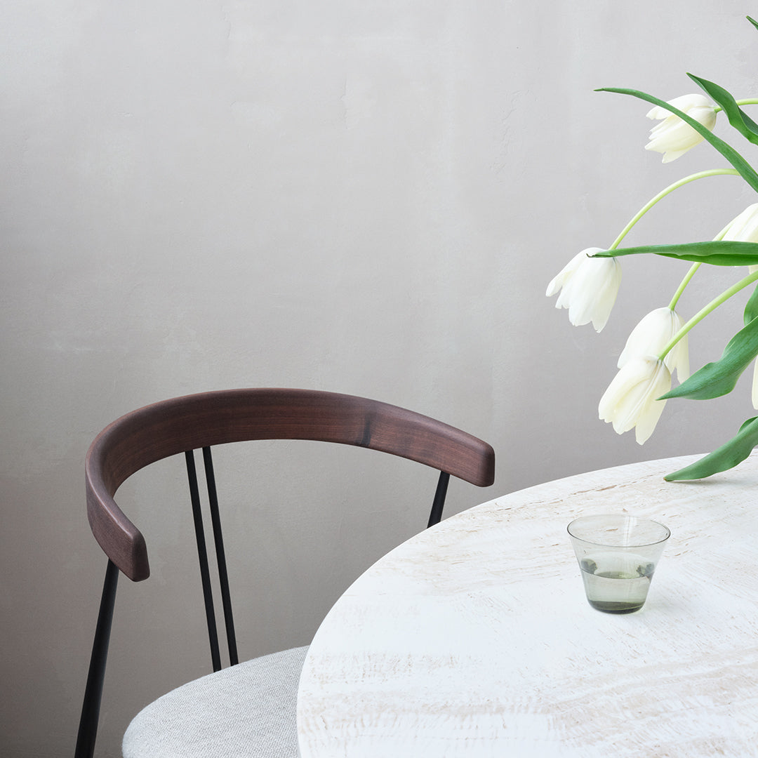 "Elegant white table with a round glass, complemented by a dark wooden chair and fresh green tulips."