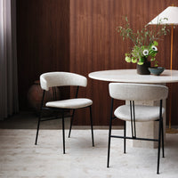Beige upholstered chairs with black metal legs, set against a warm wood-paneled wall and a light-colored round table.