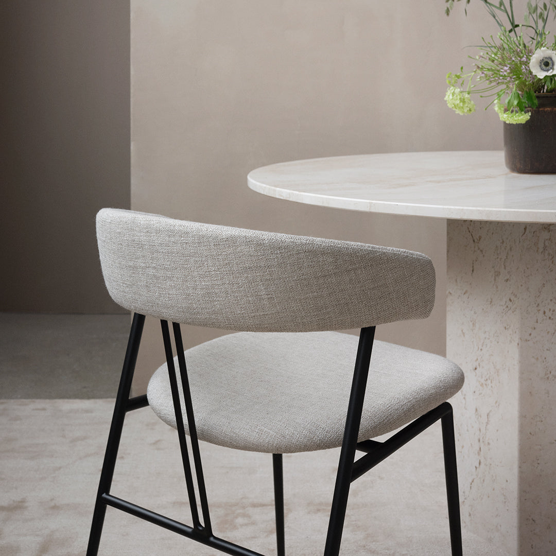 Gray upholstered chair with a sleek black frame, set against a neutral background and a round marble table.