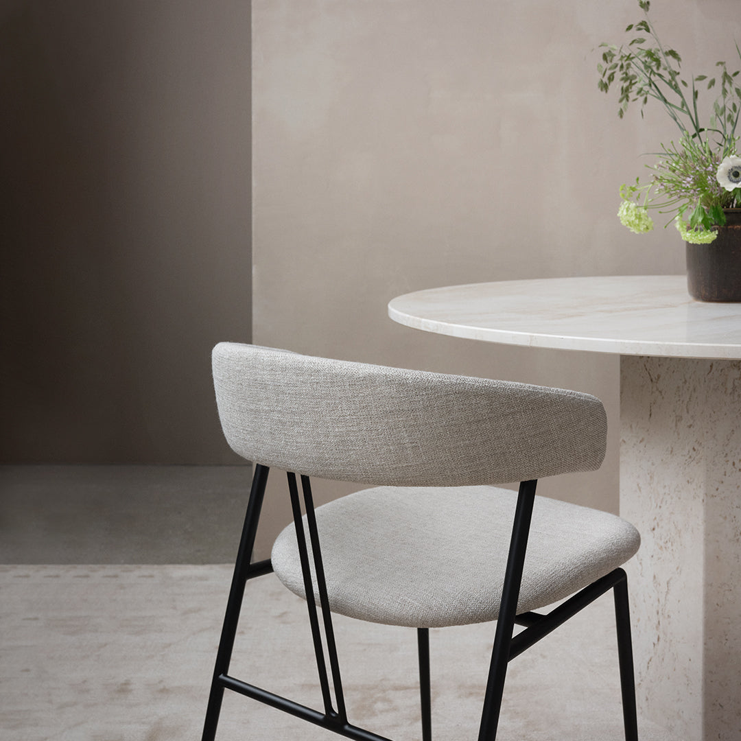 Light gray fabric chair with a sleek black frame, set against a soft beige background and a minimalist round table.