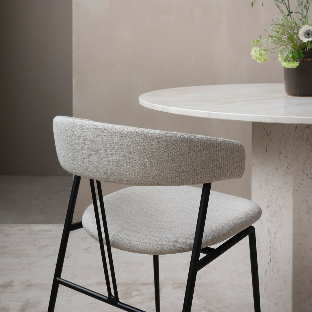 Light gray chair with a textured fabric and black metal frame, set against a neutral-toned background.
