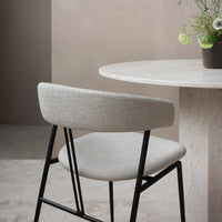 Light gray chair with a textured fabric and black metal frame, set against a neutral-toned background.