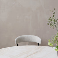 "Soft gray upholstered chair with a curved backrest, set against a muted beige wall and light marble table."