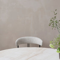 Gray upholstered chair with a curved backrest, set against a soft beige wall and a light marble table.