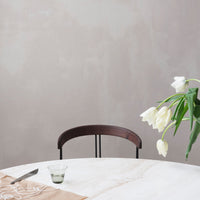 Elegant beige table with a soft marble pattern, dark wooden chair, and delicate white tulips in green vase.