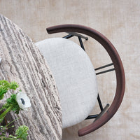 Neutral linen chair seat with a dark wood armrest, paired with a round, textured gray table against a soft beige backdrop.
