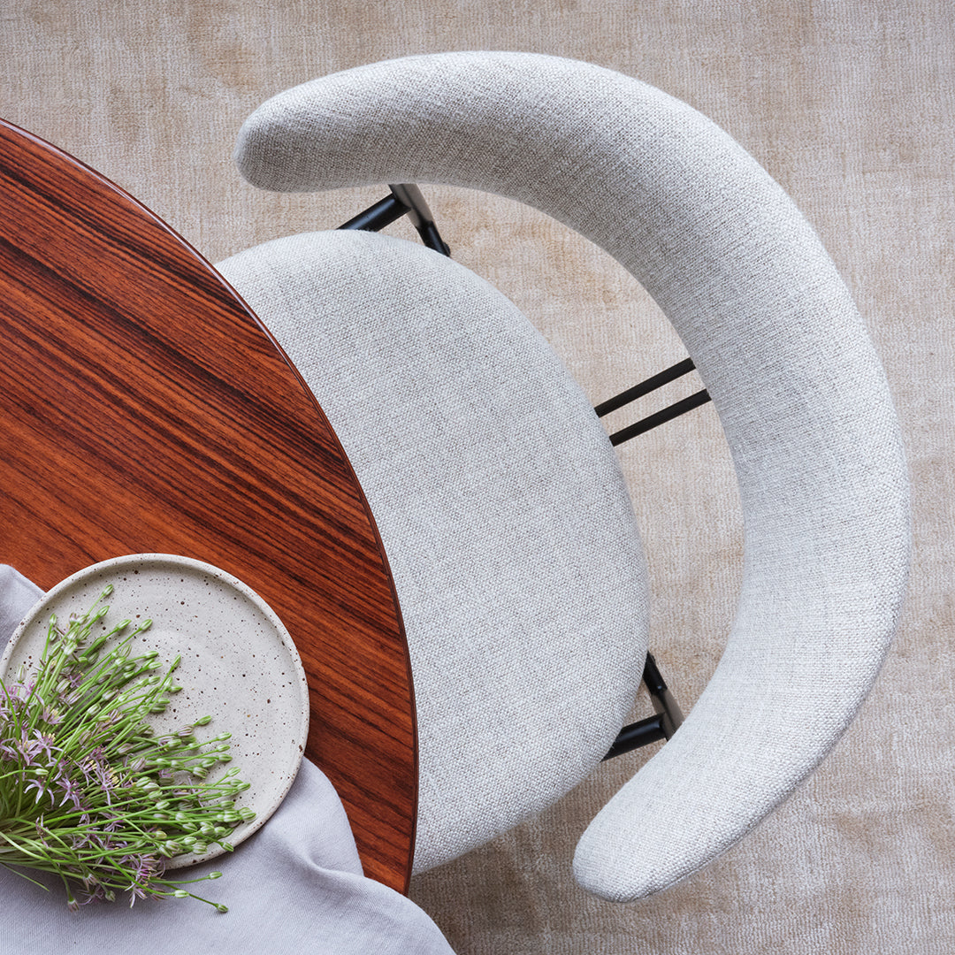 Light gray curved chair with a textured fabric pattern, paired with a rich wooden table and neutral tablecloth.