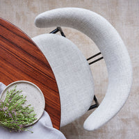Light gray curved chair with a textured fabric pattern, paired with a rich wooden table and neutral tablecloth.
